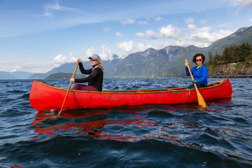 Couple adventurous female friends on a red canoe are paddling in the Howe Sound during a cloudy and...