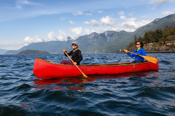 Couple adventurous female friends on a red canoe are paddling in the Howe Sound during a cloudy and sunny evening. Taken near Horseshoe Bay, West of Vancouver, BC, Canada.