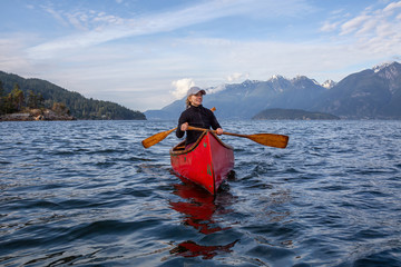 Couple adventurous female friends on a red canoe are paddling in the Howe Sound during a cloudy and...