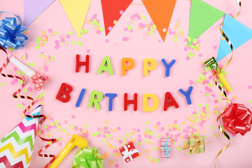 Text Happy Birthday by plastic letters with decorations and confetti on pink background