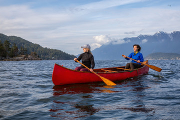 Couple adventurous female friends on a red canoe are paddling in the Howe Sound during a cloudy and...