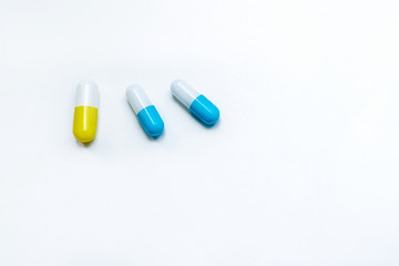 two blue capsules and one yellow capsule on a white textured background