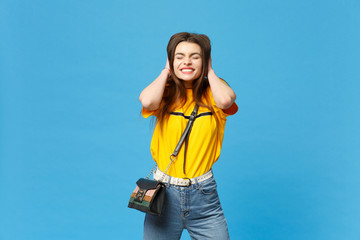 Portrait of pretty young woman in vivid casual clothes with cross body bag putting hands on head,...