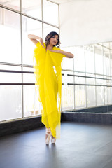 Fototapeta na wymiar Hispanic ballerina surrounded by yellow cloth standing on ends with her ballet shoes is dance studio - full body - Latin dancer