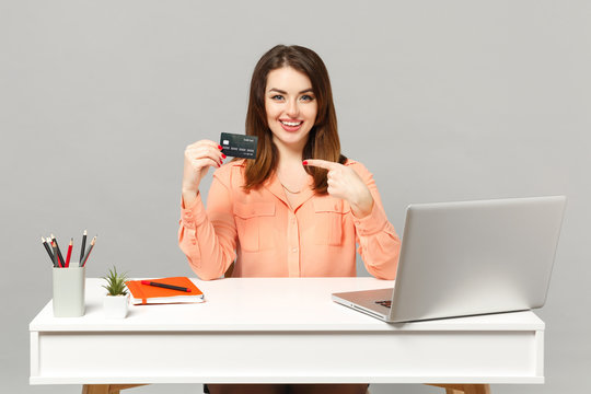 Young Cute Woman In Pastel Clothes Pointing Index Finger On Credit Bank Card Work At Desk With Pc Laptop Isolated On Gray Background. Achievement Business Career Lifestyle Concept. Mock Up Copy Space.