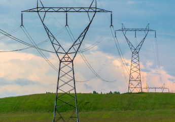 Transmission power towers over a green field awaiting a storm
