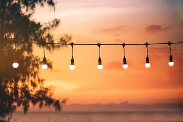 Selbstklebende Fototapeten blurred bokeh light on sunset with yellow string lights decor in beach restaurant © thanasak
