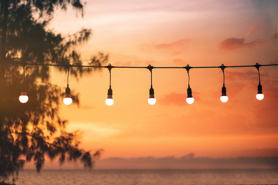 blurred bokeh light on sunset with yellow string lights decor in beach restaurant