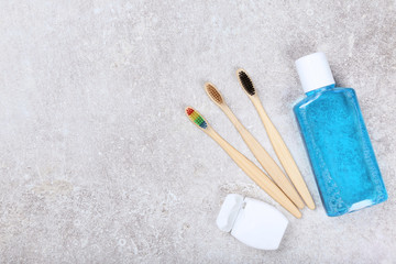 Bamboo toothbrushes with dental floss and bottle of liquid on grey background