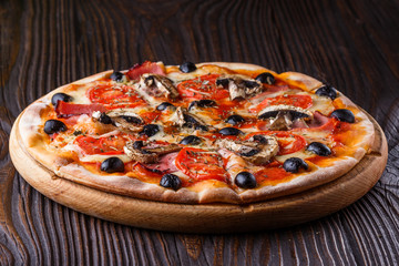 Pizza with tomato, olives, champignons, ham and cheese on round wooden plate