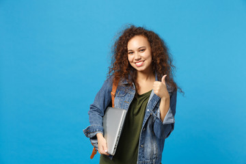 Obraz premium Young african american girl teen student in denim clothes, backpack hold pc isolated on blue wall background studio portrait. Education in high school university college concept. Mock up copy space.
