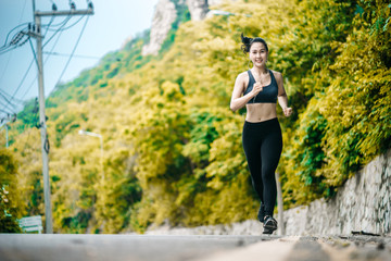 Naklejka premium An beautiful Asian woman running and listening music over road during moring. Workout and sport outdoor concept.