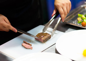 chef with knife and cutting tasty grilled steak, Chef preparing meal in the kitchen
