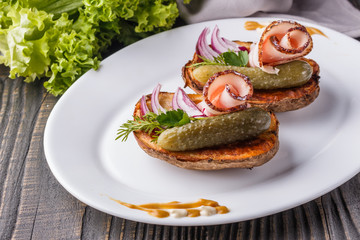 Halves baked potato with pickled cucumber, dill, salo and onion on wooden table