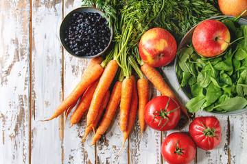 Verscheidenheid aan vers fruit, groenten en bessen wortel, spinazie, tomaten, rode appels, bosbessen over witte plank houten achtergrond. Platliggend, ruimte