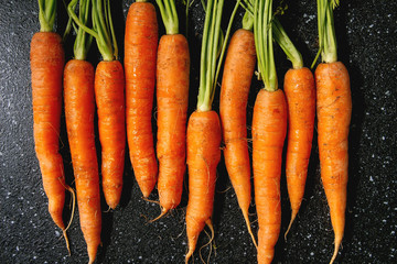 Young carrot with tops in row over black texture background. Flat lay, space. Cooking concept, food...