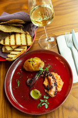 Grilled octopus on a red plate in a restaurant. Beautifully decorated dinner with white wine.Vertical.