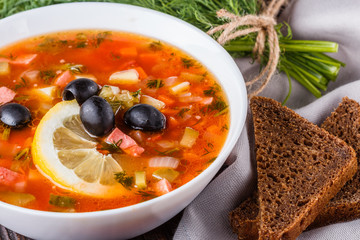 Traditional Russian meat soup Solyanka in bowl on rustic wooden table