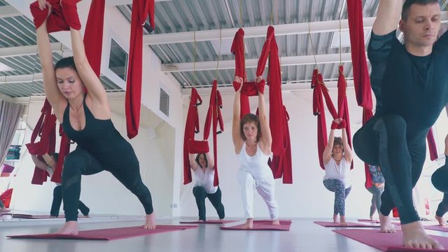 camera removes from women group standing in warrior asana and holding aero yoga hammocks low angle shot