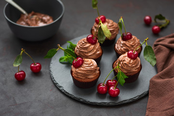 Chocolate cupcakes with ripe red cherries on dark wooden background. Selective focus. Unhealthy food.