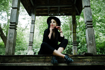 Sensual smoker girl all in black, red lips and hat. Goth dramatic woman smoking thin cigarette.