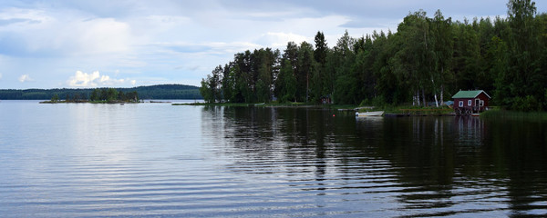Panorama view of lake Saimaa, Finland in the summer evening. Small red wooden Finnish sauna, boat...