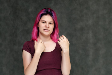 Portrait to the waist of a young pretty girl teenager in a burgundy T-shirt with beautiful purple hair on a gray background in the studio. Talking, smiling, showing hands with emotions.