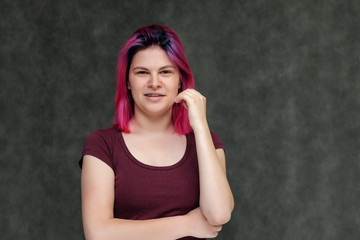 Portrait to the waist of a young pretty girl teenager in a burgundy T-shirt with beautiful purple hair on a gray background in the studio. Talking, smiling, showing hands with emotions.