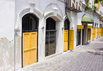 Fototapeta na wymiar Empty sidewalk near a wall historic colonial-style building with wooden shutters and bars on windows on a hot sunny day in the old district of Kuala Lumpur, Malaysia