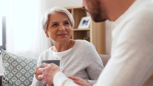 family, generation and people concept - happy smiling adult son bringing coffee to senior mother at home