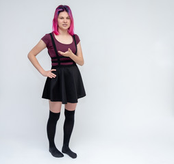 Full-length portrait of young pretty teenager girl in burgundy T-shirt and black dress with beautiful purple hair on a white background in the studio. Talking, smiling, showing hands with emotions.