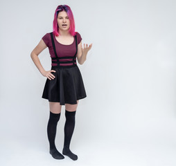 Full-length portrait of young pretty teenager girl in burgundy T-shirt and black dress with beautiful purple hair on a white background in the studio. Talking, smiling, showing hands with emotions.