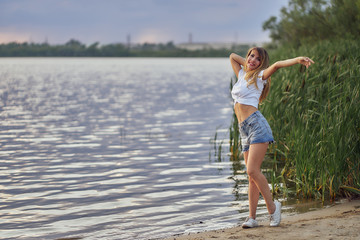 slim girl in shorts and white T-shirt stands by the water on the lake