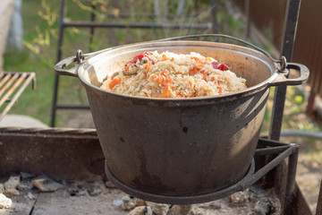 Cooking tasty pilaf in nature. Cooking pilaf in big cauldron on fire at picnic. Cooking pilaf in a pot on the fire close up.