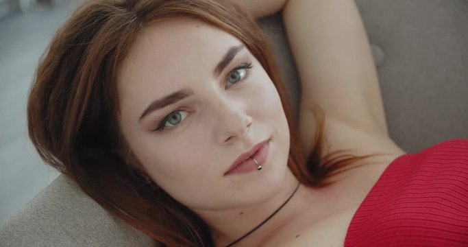 Closeup shoot of young sexy caucasian female in red two-piece lingerie looking at camera and posing laying on the couch indoors
