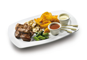 Solomillo con patatas y verduras acompañada de salsas. Sirloin steak with potatoes and vegetables accompanied by sauces.