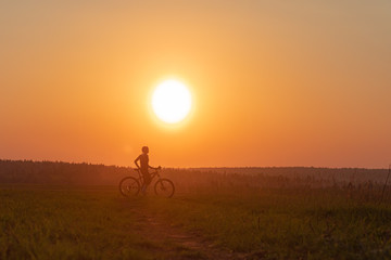Fototapeta premium Happy girl with a bicycle on the nature on the background of bright sunset and yellow sun