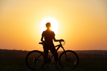 Fototapeta premium Happy girl with a bicycle on the nature on the background of bright sunset and yellow sun