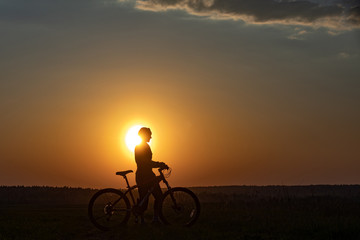 Fototapeta premium Happy girl with a bicycle on the nature on the background of bright sunset and yellow sun