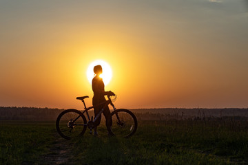 Happy girl with a bicycle on the nature on the background of bright sunset and yellow sun