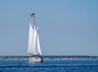 Three-masted sailboat under full sail with American flag flying prominently off Cape Cod coast