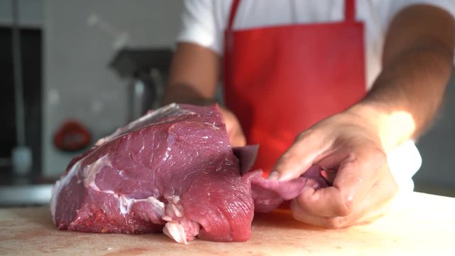 El carnicero está cortando la carne con mucho cuidado.
