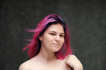 Naklejka premium Close-up portrait of a young pretty teen girl with beautiful purple hair on a gray background in the studio. Smiles with emotions