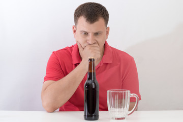 man sitting at a table with a mug of beer, struggling with alcohol addiction