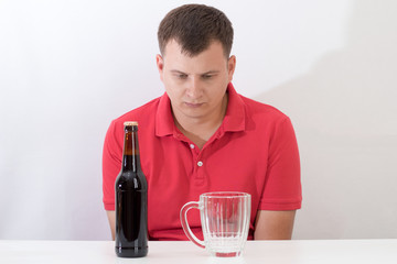 man sitting at a table with a mug of beer, struggling with alcohol addiction