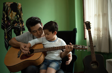 Obraz premium Parent Homeschooling Concept - Asian Family, Father are Teaching Little Boy Playing Guitar and Sing a Song in Music Time , Education Setting and Planning at Home