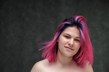 Naklejka premium Close-up portrait of a young pretty teen girl with beautiful purple hair on a gray background in the studio. Smiles with emotions