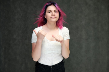 Portrait to waist of a young beautiful girl teenager in a white T-shirt with beautiful purple hair on a gray background in the studio. They say, they smile, they show hands with emotions.