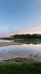 calm lake after sunrise with dead log in foreground. tranquil blue sky with hints of color