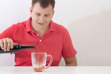 Happy man pouring a dark beer into a mug from a glass bottle